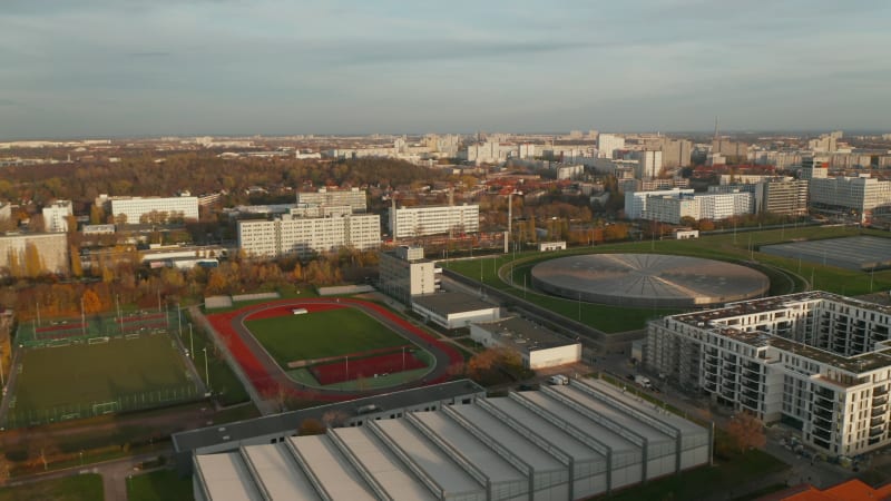 Red Running Track sports field in Urban City Area with futuristic Velodrome Building cycling Arena in Berlin, Germany, Aerial slide dolly left at Sunset