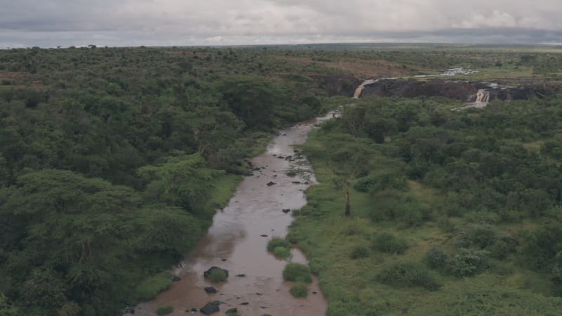 Brown river with waterfall surrounded by tropical vegetation