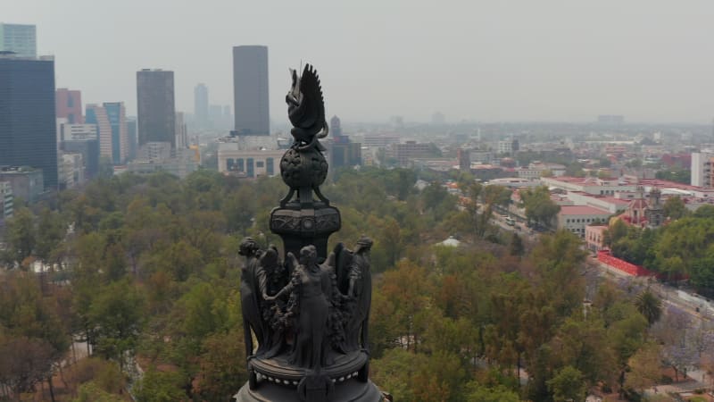 Drone flying around statues on memorial located on high pillar. Circular view of figures and Mexico city panorama. Variety of building in town.