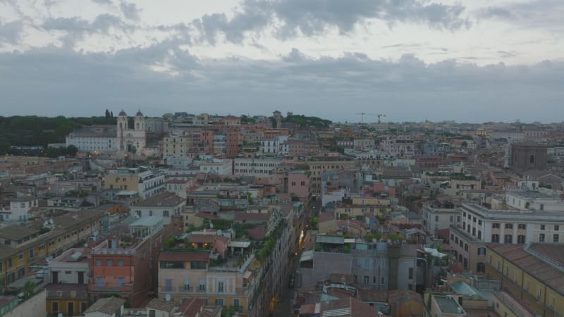 Fly above town development, old apartment buildings with rooftop terraces and tourist landmarks at dusk. Rome, Italy