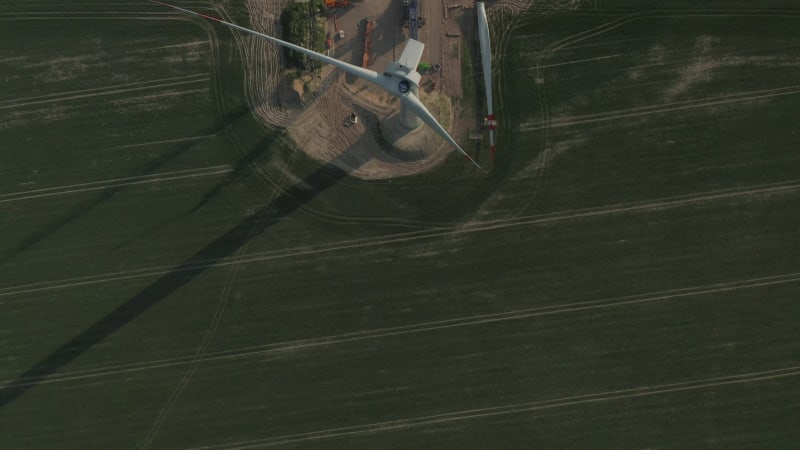 Close overhead drone view flight over Wind Turbine under construction being built on rich green agriculture field