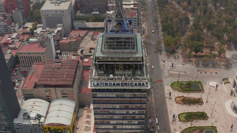 Drone camera flying backwards and tilting up. Close-up view of number clock on top of tall building changing to panoramic view of Mexico city downtown with strongly polluted air.