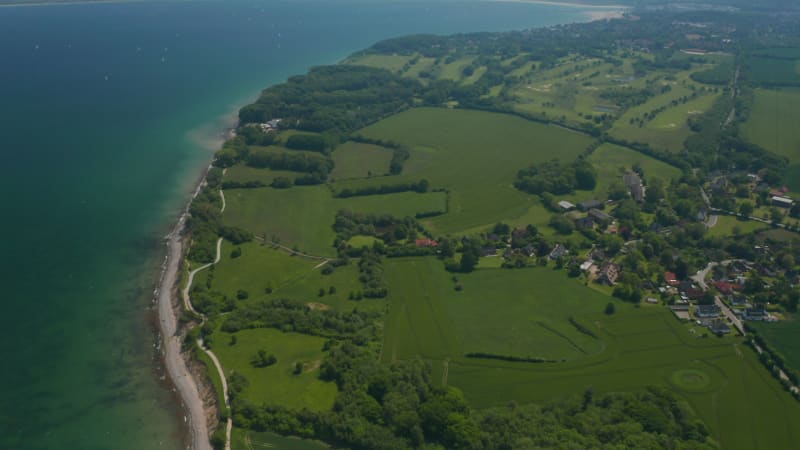 Amazing high aerial view of green countryside fields facing turquoise Baltic sea, tilt up, sunny day