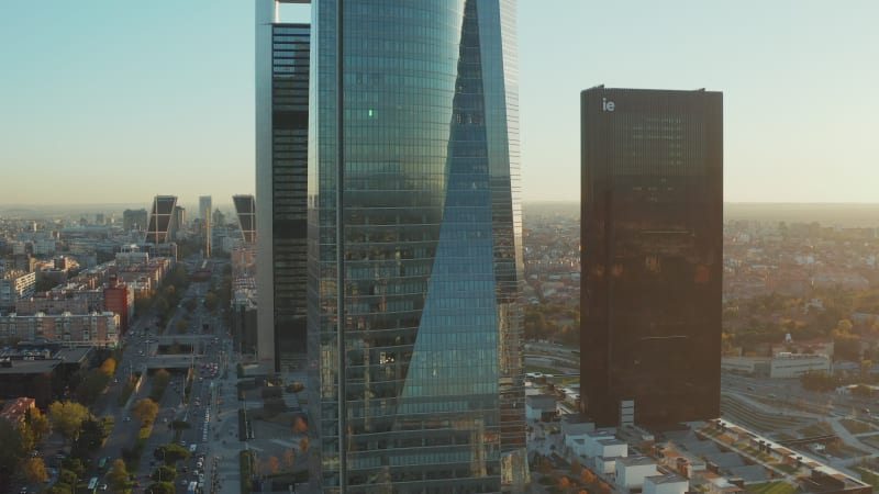 Slide and pan footage of modern buildings in Cuatro Torres Business Area. Glossy glass facades of skyscrapers reflecting surroundings.