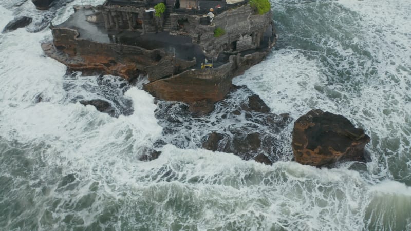 Aerial view of dangerous rocks and strong waves crashing into off shore cliff with Tanah Lot temple  in Bali, Indonesia