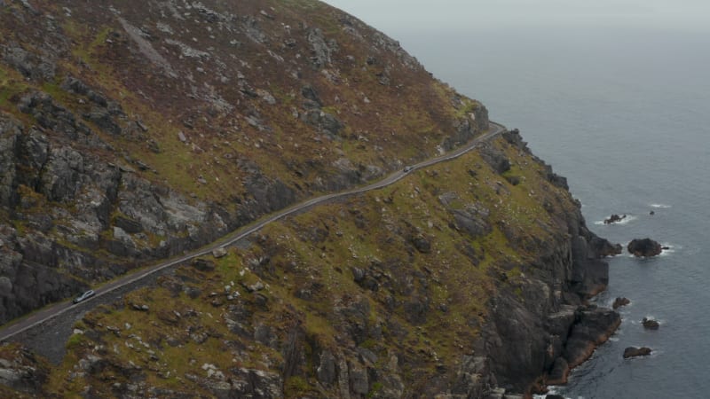 Breath taking shot of slowly moving car on narrow panoramic route in steep slope above sea coast. Dangerous road around Slea Head. Ireland