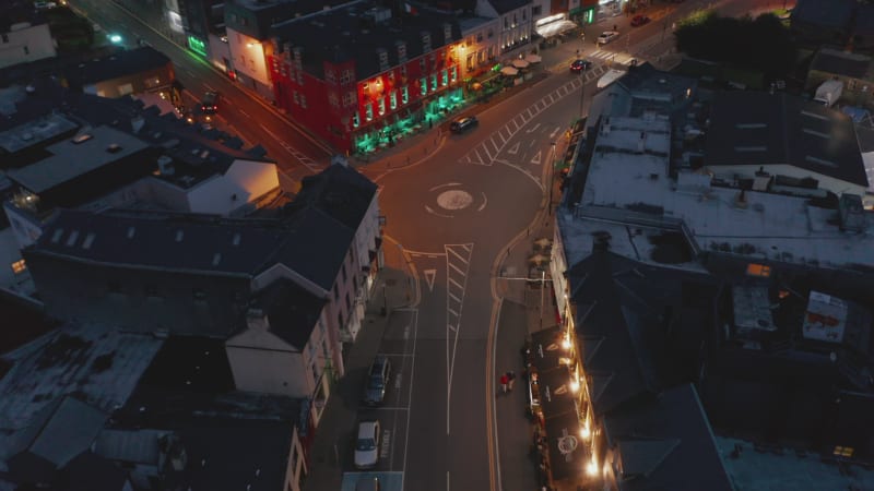 Fly above illuminated street in city. Colourful house facades along road in town centre at night. Killarney, Ireland