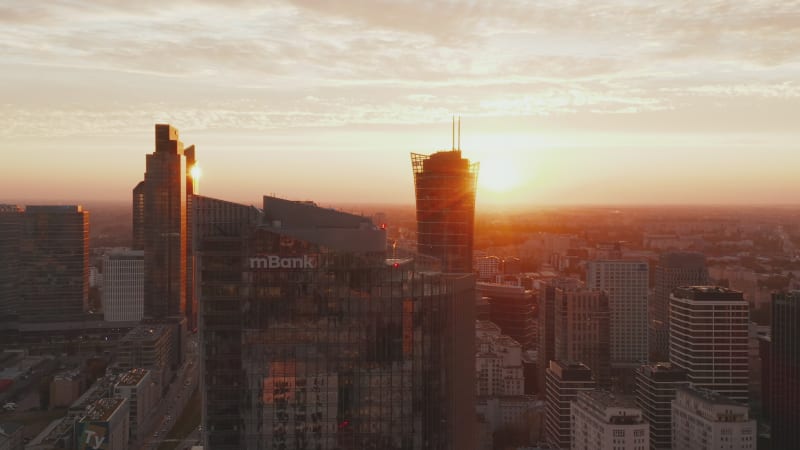 Slider of modern office high rise building and group of downtown skyscrapers in background against bright sun. Warsaw, Poland