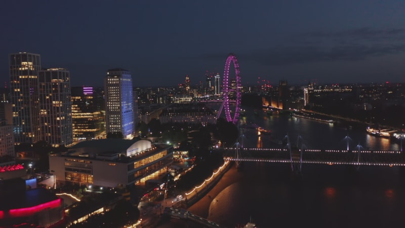 Ascending footage of Thames river south bank at night. Royal Festival Hall and London eye. Aerial view at colourful city lights. London, UK