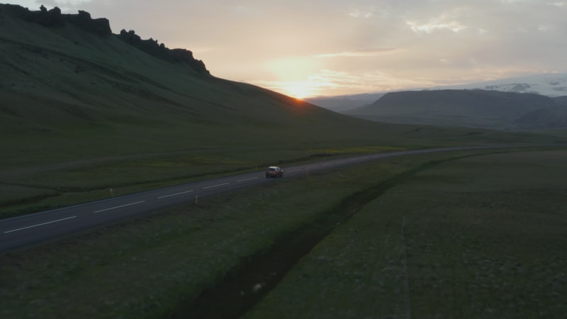 Birds eye view car peacefully driving on ring road, the most important highway in Iceland. Aerial view car driving along empty country road at golden sunset