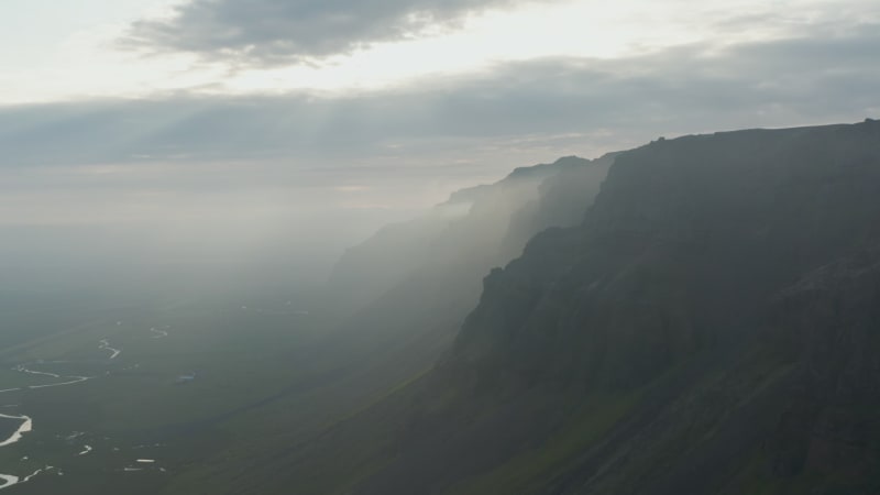 Aerial panoramic view of scenic Icelandic nature. Flying close to tall mountains with sunrays coming trough dark clouds.