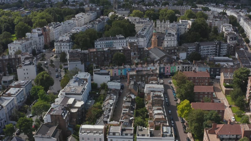 Slide and pan shot of church tower among town houses in urban neighbourhood. Aerial view of residential district in city. London, UK