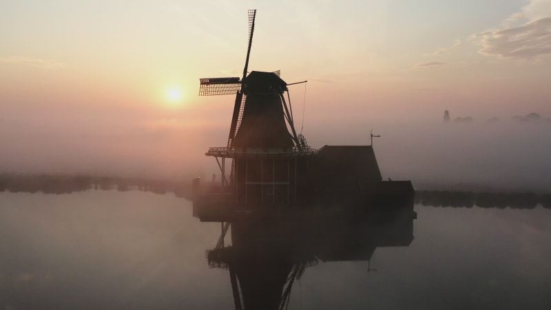 Silhouette of a windmill by the water surrounded by fog