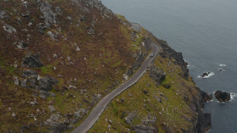 High angle view of car passing curve and narrow road high above sea coast. Amazing panoramic route. Ireland