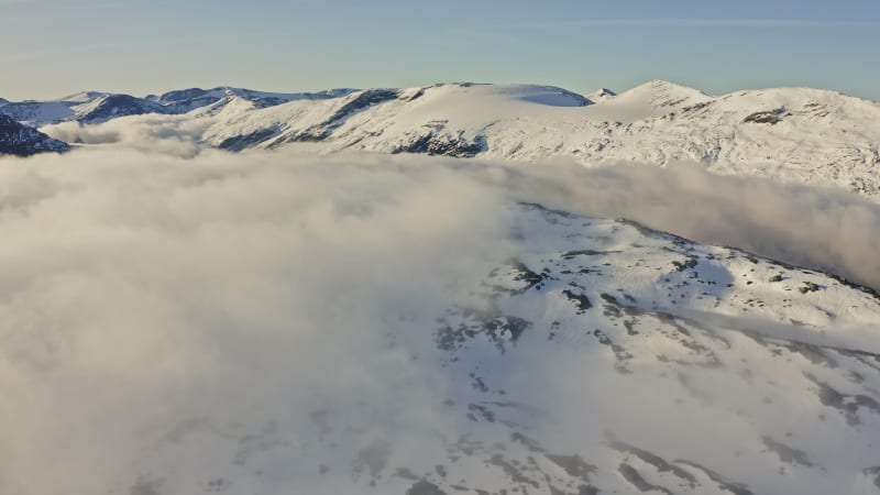 Cloud cover across snow covered mountaintops on a clear day in Norway.