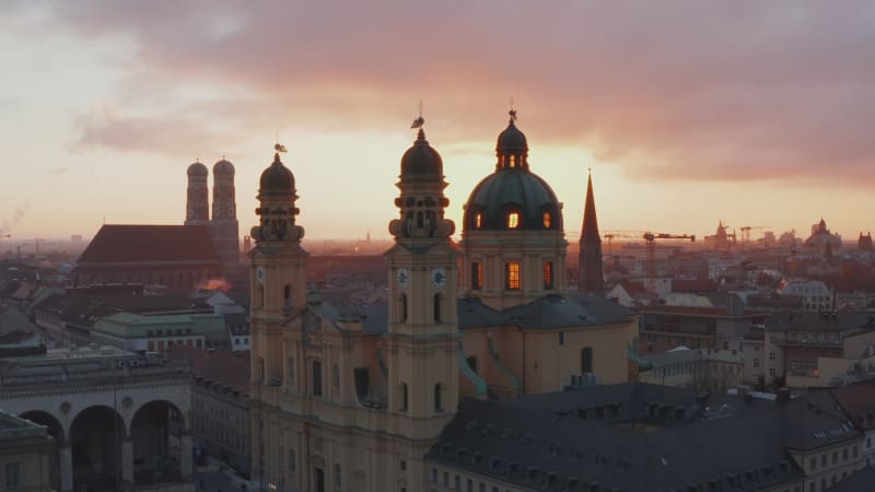 Aerial Slide by Stunning Yellow Theatine Church Cathedral Building in Golden Hour Sunset light, Munich Cityscape in distance