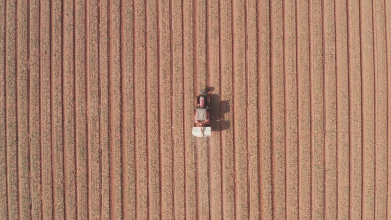 Tractor hauling a Two disc Fertilizer spreader in a large field, Aerial follow footage.