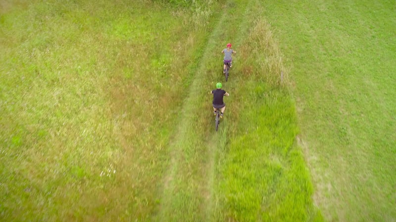 Aerial view of man and woman cycling in the forest on dirt road.