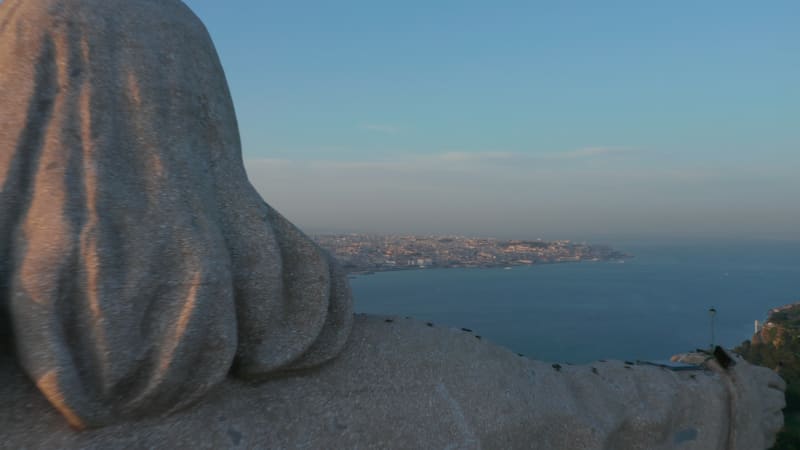 Close up back aerial view of Sanctuary of Christ the King statue on the hill with reveal of urban city center of Lisbon on the sea coast