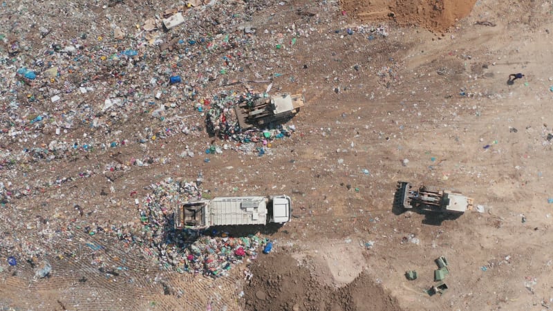 Top down aerial footage of a Municipal Solid waste Landfill during collecting, sorting and pressing work, with a massive flock of birds.