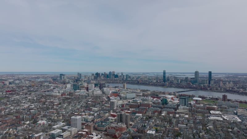 Fly above large city. Wide river flowing through metropolis. Evening aerial shot of town development. Boston, USA