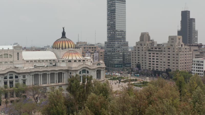 Reveal of city, ascending drone flying around colourful dome with bird sculpture of Palace of fine arts (Palacio de Bellas Artes) in historic city. Mexico City, Mexico.