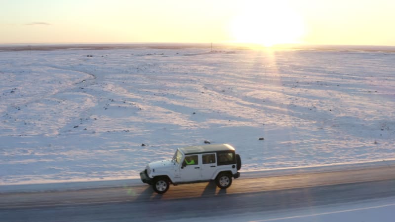 AERIAL: Close up following Jeep from side on snow road in Iceland at Sunset Winter, Sun, Arctic