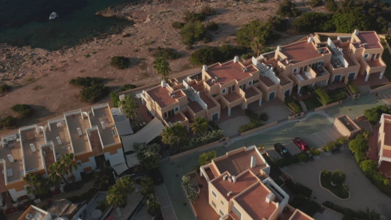 Aerial view of rooftop of beautiful houses in colony near to the beach and shore surrounded by ocean and mountain in Ibiza in Spain during an early morning