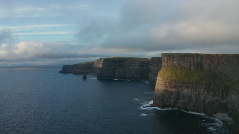 Romantic evening panoramic shot of high cliffs at sunset. Vertical rock walls above ripples sea surface. Cliffs of Moher, Ireland