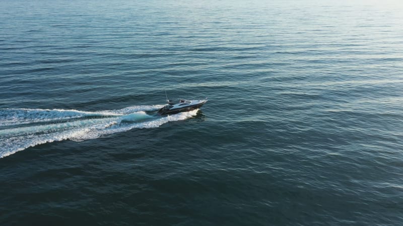 Aerial view of a speedboat sailing at sunset into the sea.