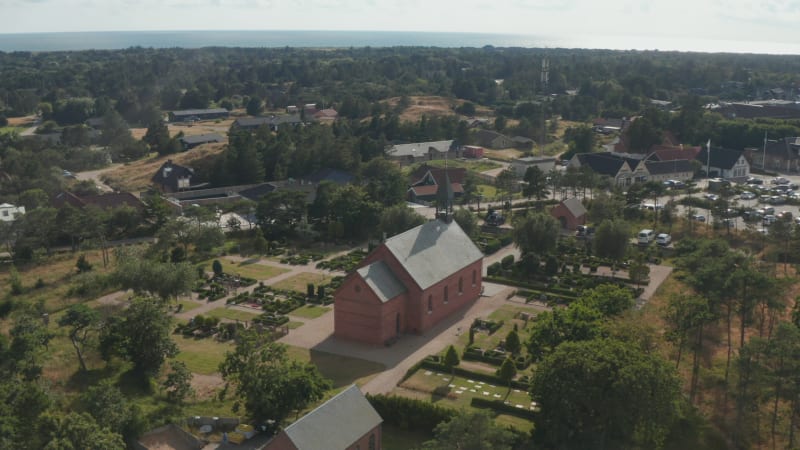 Slide and pan shot of wooden chapel in middle of graveyard. Panoramic footage of coastal landscape around Oksby. Denmark