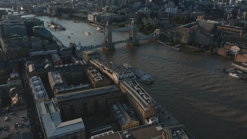 Tilt up reveal of Tower Bridge across River Thames and group of modern office buildings in City financial hub in golden hour. London, UK