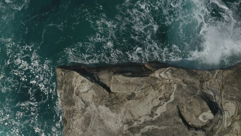 Aerial Overhead Top Down Birds Eye View of Big Ocean Waves crashing on Rocks