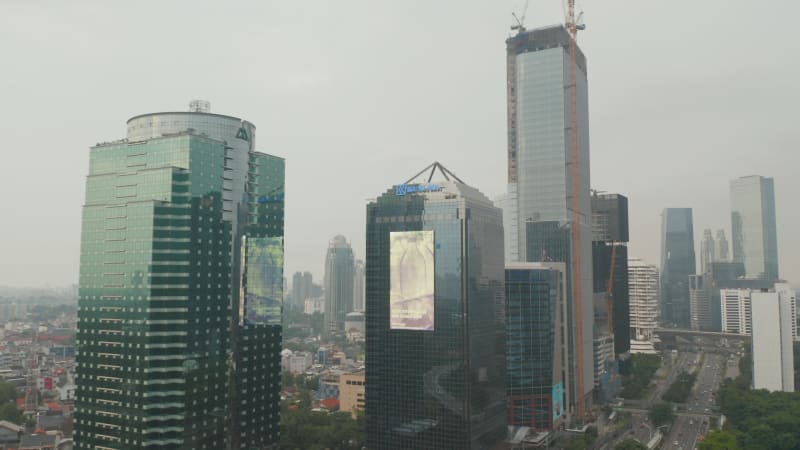 Static aerial shot of large commercial display with moving commercial ads on the side of a glass skyscraper in urban city center