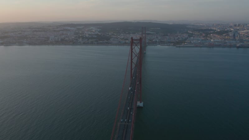 Evening aerial view of 25th of April Bridge connecting Lisbon and Almada. Long cable-stayed highway bridge over Tegus river. Drone rotating around. Lisbon, capital of Portugal.