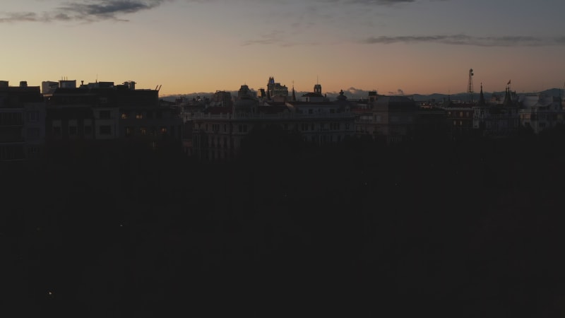 Rising shot of dim buildings in urban neighbourhood. Revealing evening cityscape against romantic golden sunset sky.