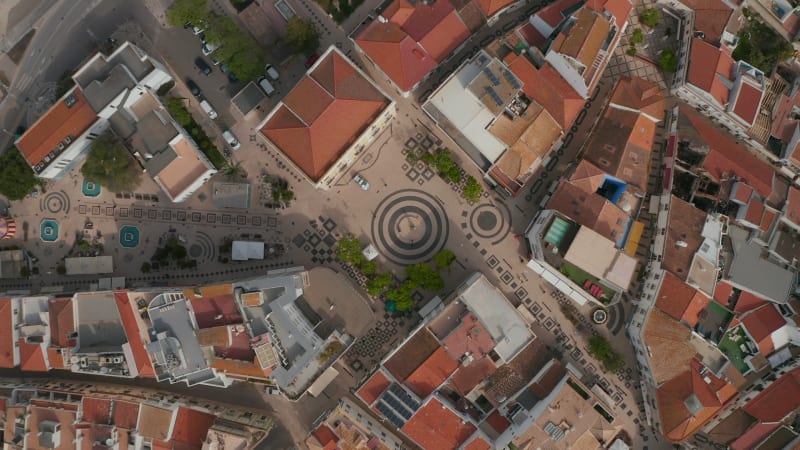 Gil Eanes square and rooftops houses in Lagos, Algarve, Portugal, aerial birds eye overhead top down view, drone rises up reveal scenic cityscape with people walking on streets, day