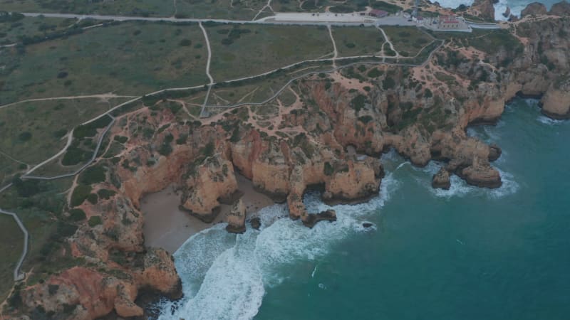 Establishing aerial drone view of scenic outdoor coastline in Lagos, Portugal, circling pan above Atlantic ocean, cloudy day