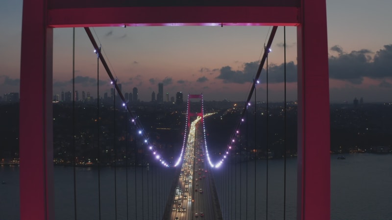 Epic Dolly forward through Istanbul Bosphorus Bridge Arch Illuminated in Red light at Night with Car traffic, Aerial Drone