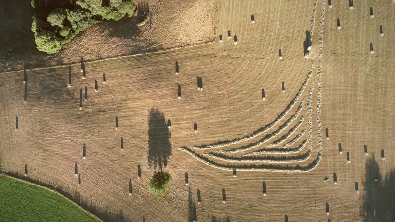 Abstract aerial view of tractor harvesting straw bales in field.