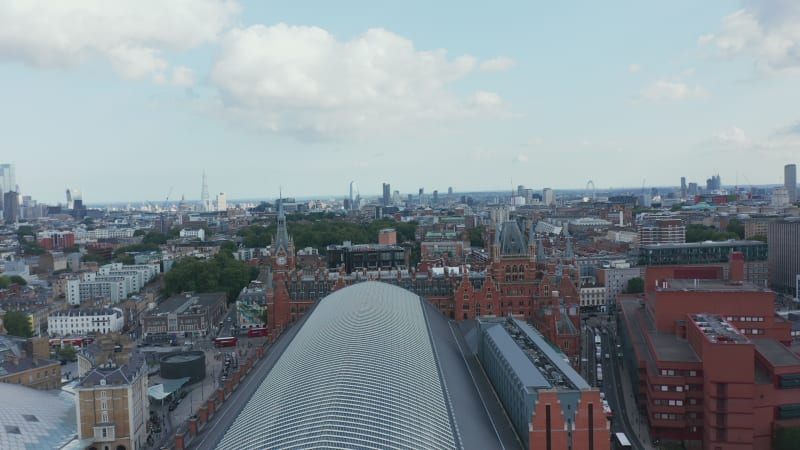 Backwards fly above large building of St Pancras train station. Aerial view of roof over platforms in transport terminal. London, UK