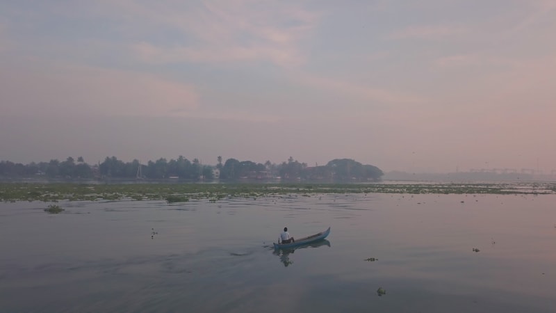 Man rowing a canoe in the ocean near a fishing village