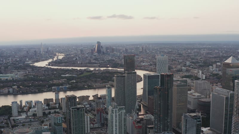 Sliding reveal of modern business borough. Aerial view of tall futuristic office buildings in Canary Wharf financial centre towering above city.  London, UK