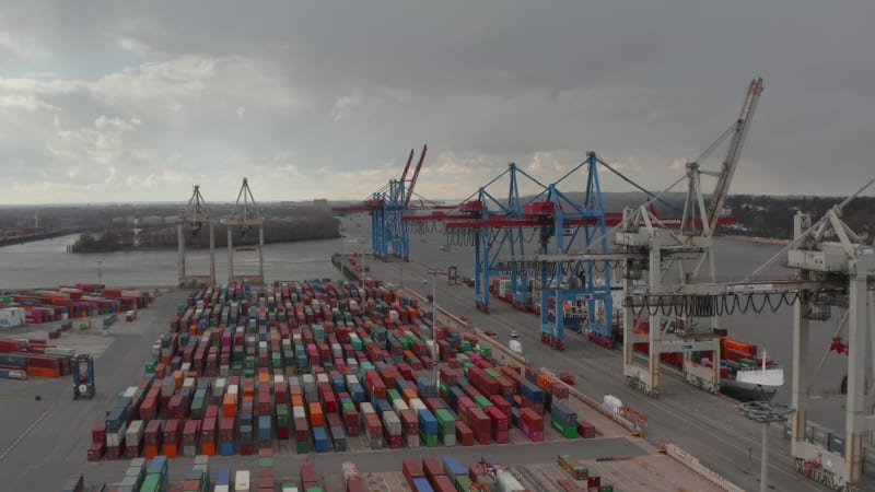 Slow aerial dolly in view of large cargo cranes above rows of colorful containers in Hamburg industrial port