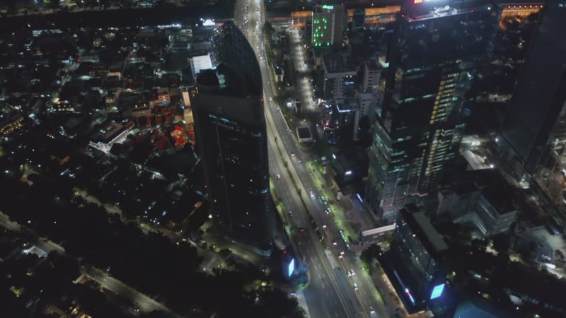 Aerial tilting shot following busy traffic on multi lane road through downtown Jakarta at night