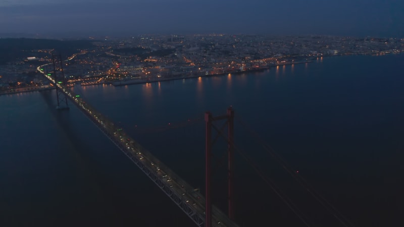 Night aerial panorama of urban city center of Lisbon in lights with Ponte 25 de Abril red bridge crossing the sea