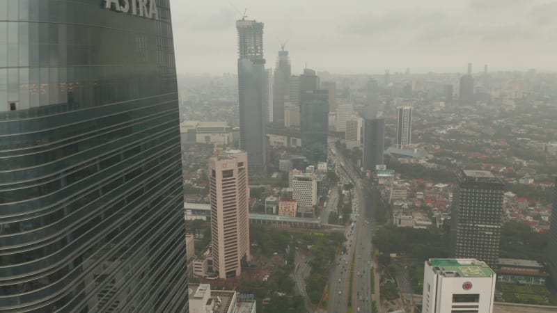 Aerial view reveal flying from behind a skyscraper to wide view of Jakarta city skyline reveal in cloudy weather