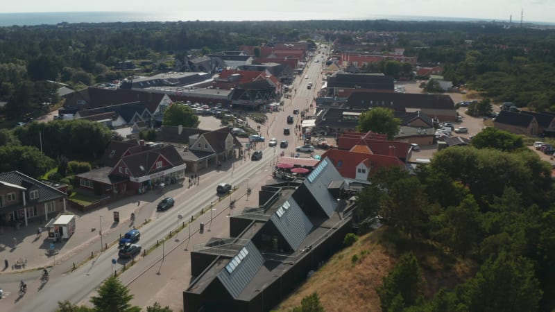 Backwards fly above buildings along main street in Oksby. Aerial view of small town near sea coast. Summer vacation destination. Denmark