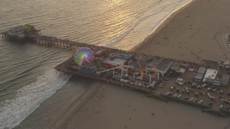 Pacific Park Theme Park on Santa Monica Pier with Ferris Wheel in beautiful Golden Hour Sunset light over coastline, Wide Angle Shot, Lowering crane down