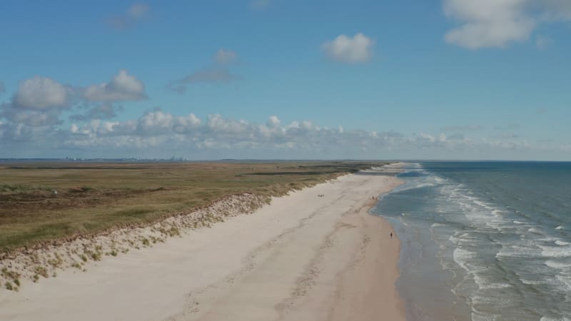 Rising shot of white sand beach and coastal landscape. Aerial shot of sea washing coast of Jutland. Denmark